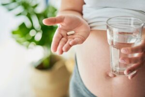 A pregnant woman holding vitamins and water